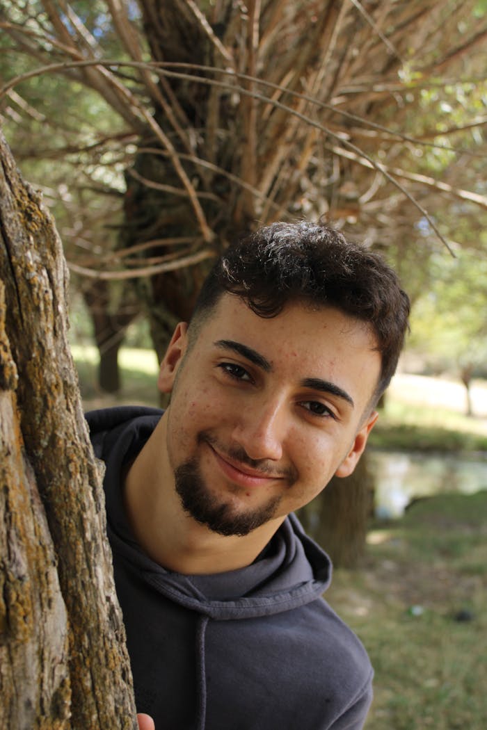 gallery-03 Portrait of a smiling young man peeking from behind a tree in a park in Nevşehir, Türkiye.
